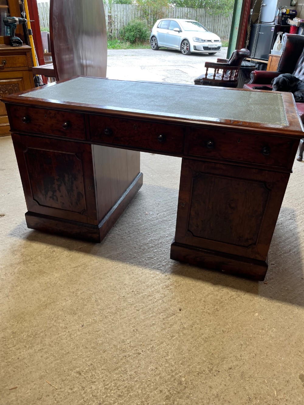 A nineteenth-century Victorian burr walnut pedestal desk featuring a green leather writing surface, multiple drawers with turned wooden handles, and a plinth base. View VI