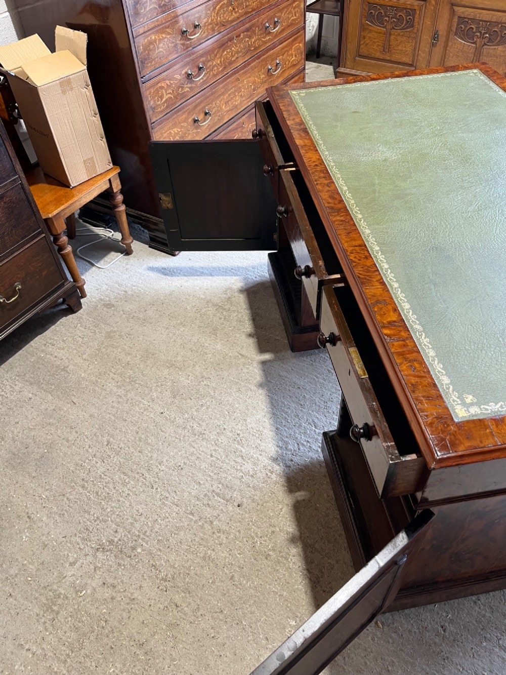 A nineteenth-century Victorian burr walnut pedestal desk featuring a green leather writing surface, multiple drawers with turned wooden handles, and a plinth base. View VII
