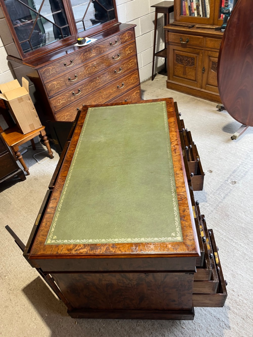 A nineteenth-century Victorian burr walnut pedestal desk featuring a green leather writing surface, multiple drawers with turned wooden handles, and a plinth base. View IX
