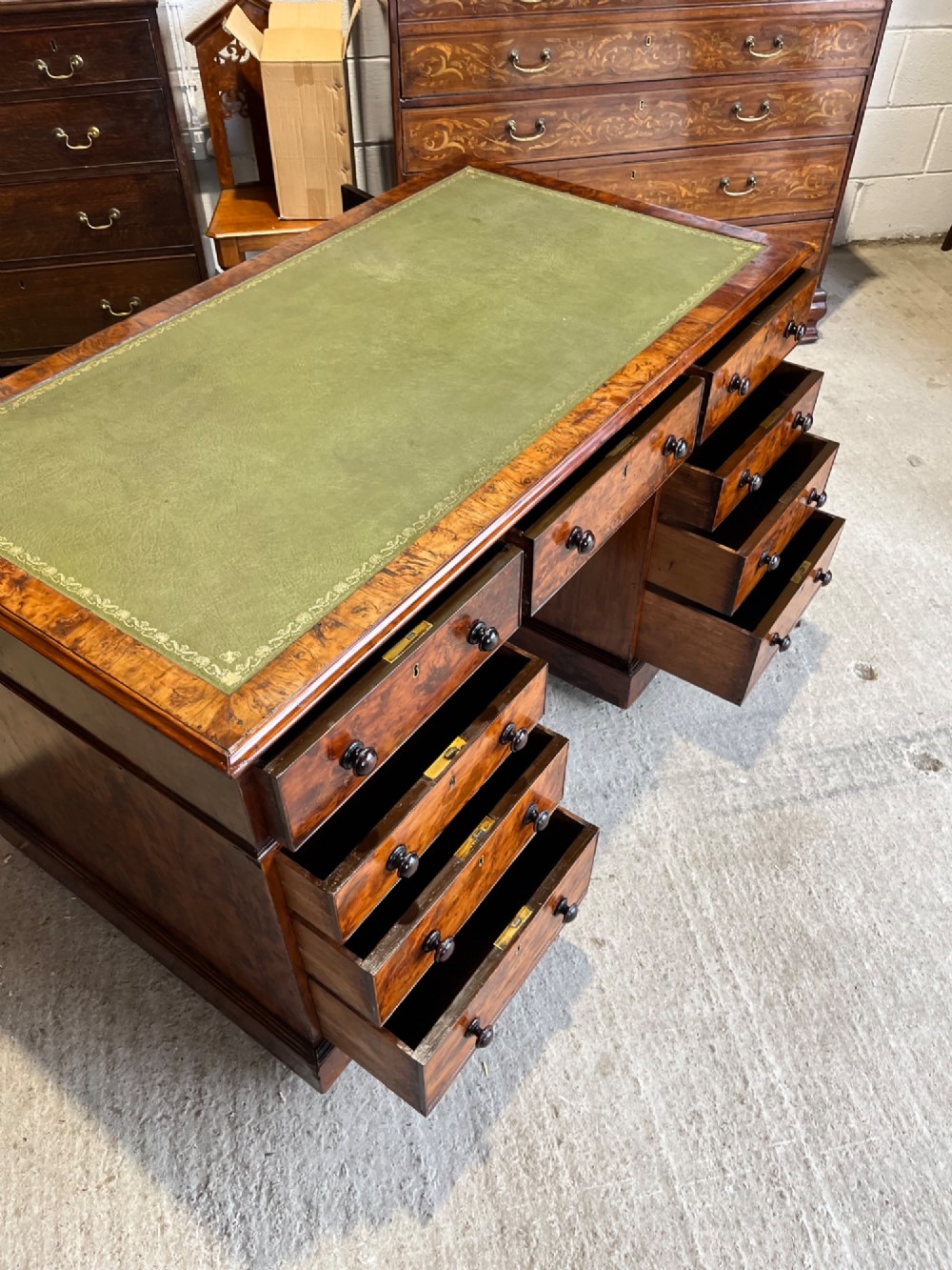 A nineteenth-century Victorian burr walnut pedestal desk featuring a green leather writing surface, multiple drawers with turned wooden handles, and a plinth base. View X