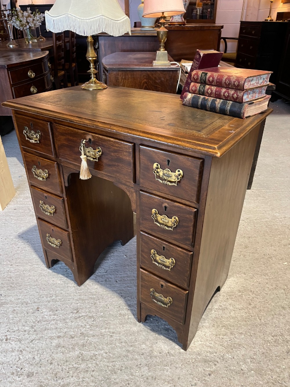 A late 19th-century dark mahogany kneehole desk featuring nine drawers with decorative brass handles and a central kneehole recess. View VI