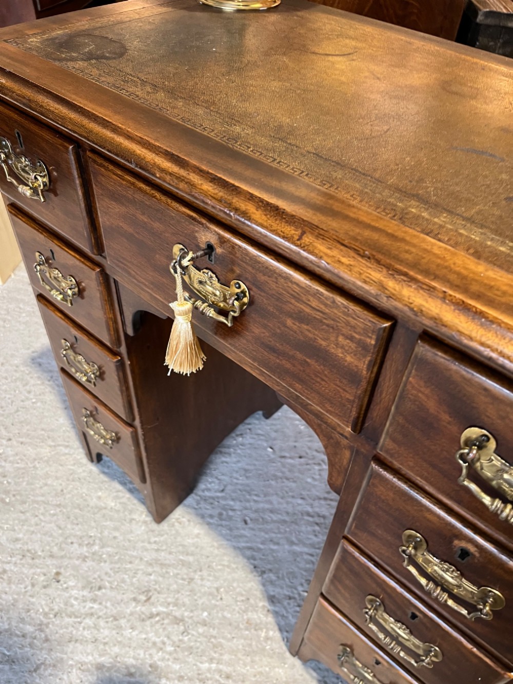 A late 19th-century dark mahogany kneehole desk featuring nine drawers with decorative brass handles and a central kneehole recess. View VIII