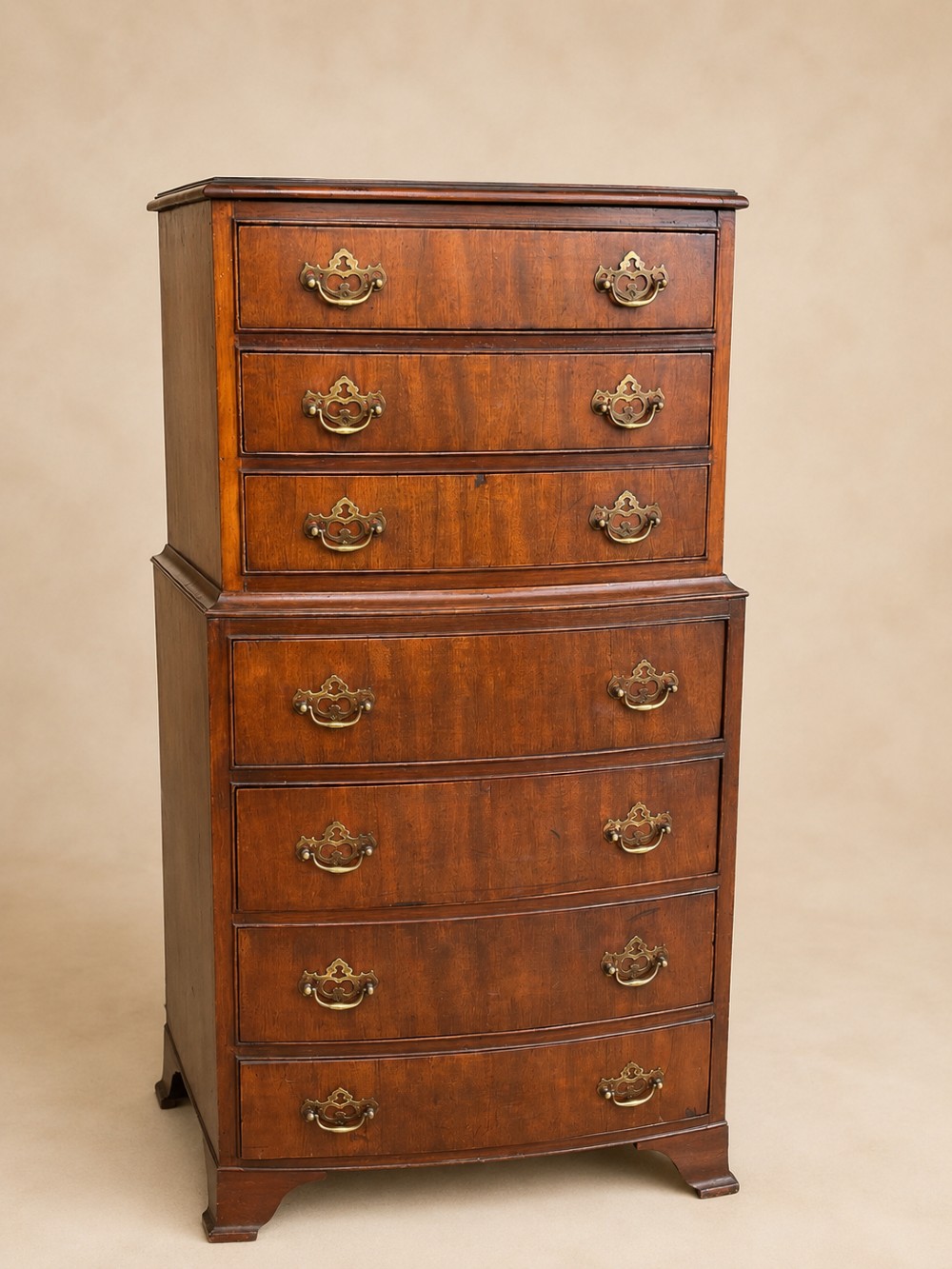 An antique mahogany bowfront chest on chest featuring seven graduated drawers with brass handles and splayed bracket feet against a plain background. View II
