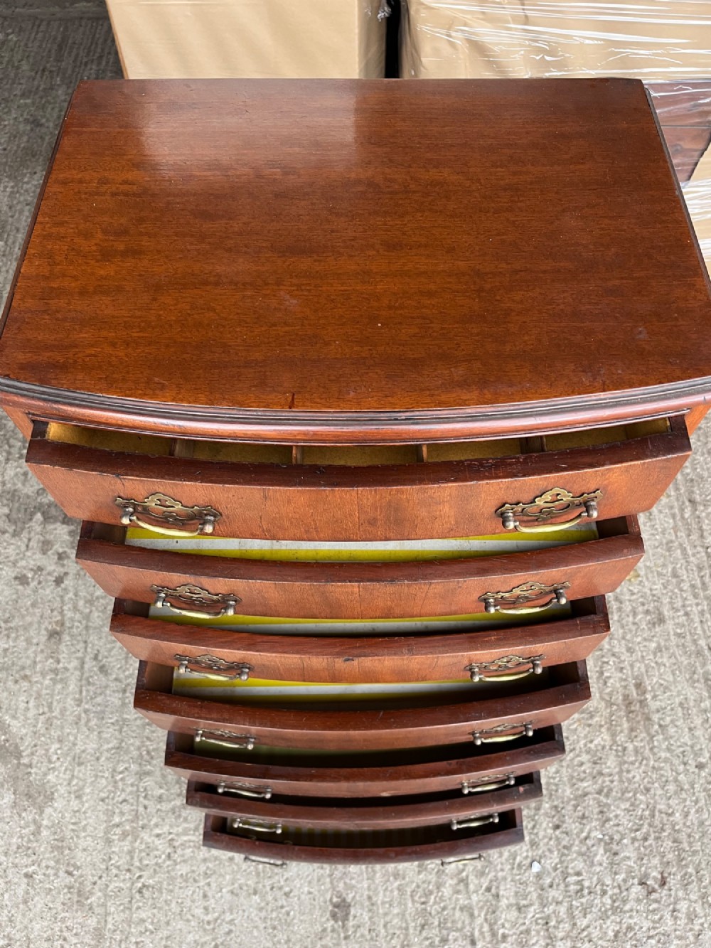 An antique mahogany bowfront chest on chest featuring seven graduated drawers with brass handles and splayed bracket feet against a plain background. View V
