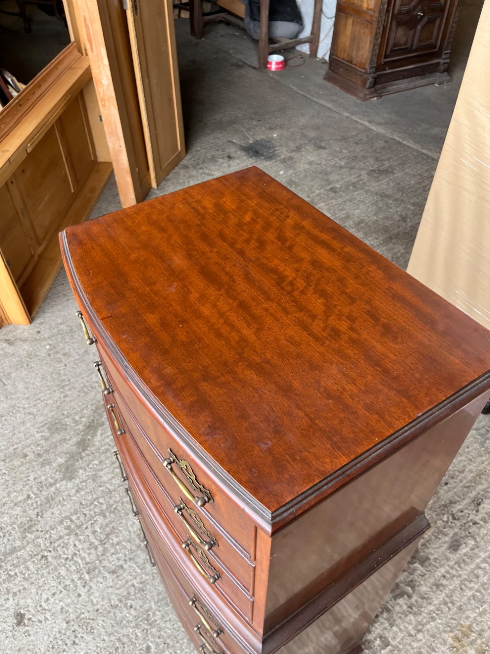 An antique mahogany bowfront chest on chest featuring seven graduated drawers with brass handles and splayed bracket feet against a plain background. View VI