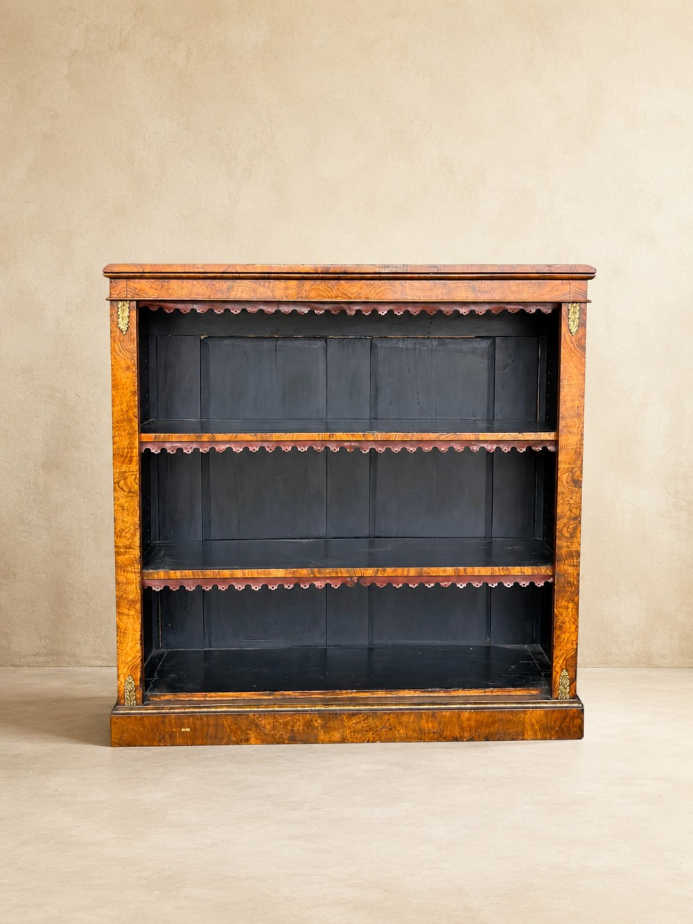 A 19th-century open walnut bookcase featuring highly figured veneer, brass corner mounts, three shelves with scalloped trim, and a dark painted back panel. View II