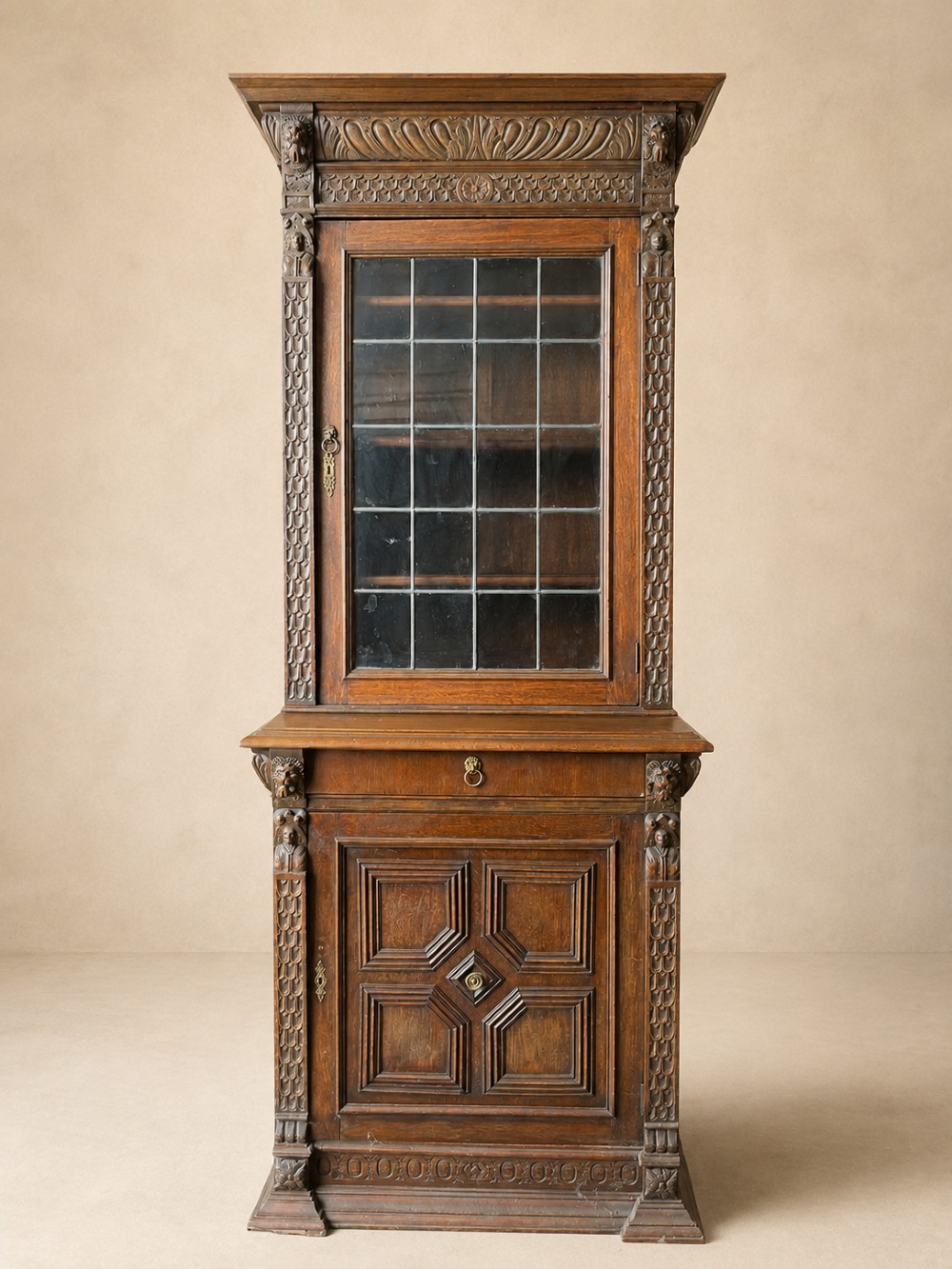 A slim 19th-century carved oak bookcase featuring a single leaded glass upper door, a central drawer, and a lower carved cupboard door with geometric panels.