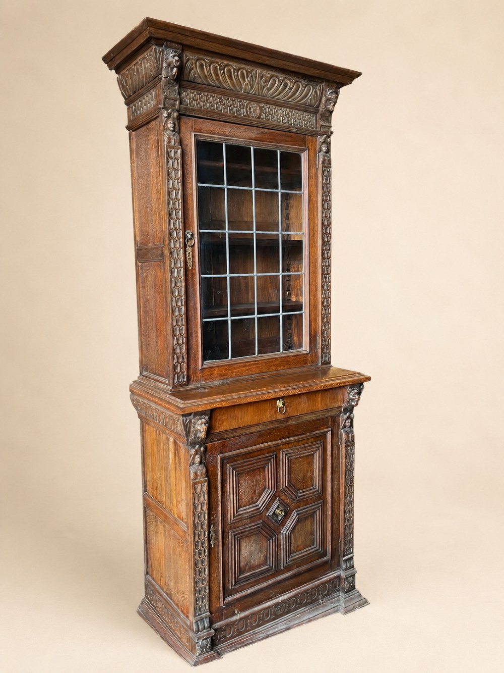 A slim 19th-century carved oak bookcase featuring a single leaded glass upper door, a central drawer, and a lower carved cupboard door with geometric panels. View III