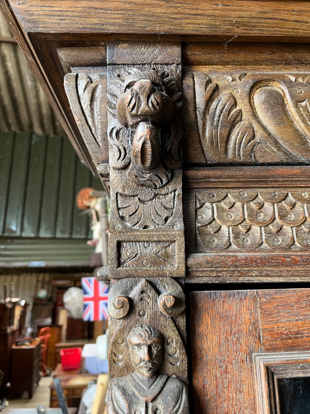 A slim 19th-century carved oak bookcase featuring a single leaded glass upper door, a central drawer, and a lower carved cupboard door with geometric panels. View VI