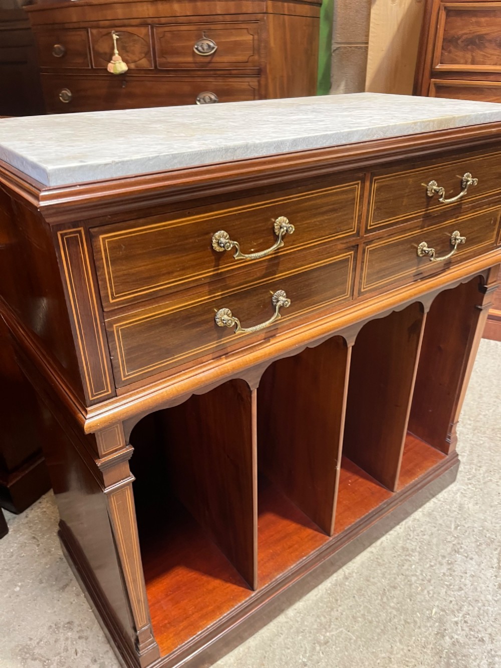 A late 19th-century inlaid mahogany cabinet featuring a grey marble surface, four drawers with string inlay and brass drop handles, above four vertical open storage divisions. View IV