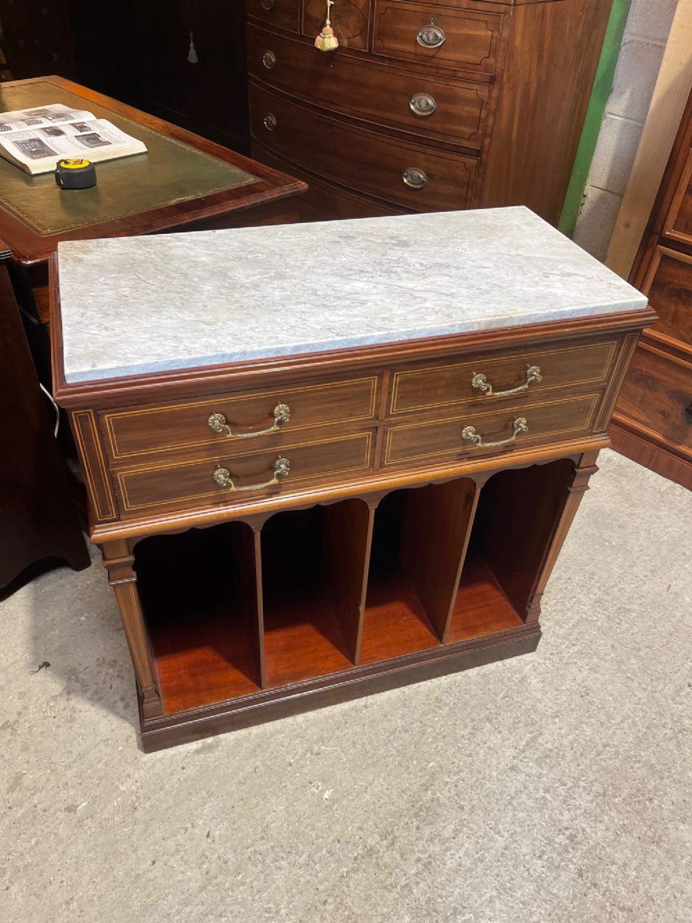 A late 19th-century inlaid mahogany cabinet featuring a grey marble surface, four drawers with string inlay and brass drop handles, above four vertical open storage divisions. View V