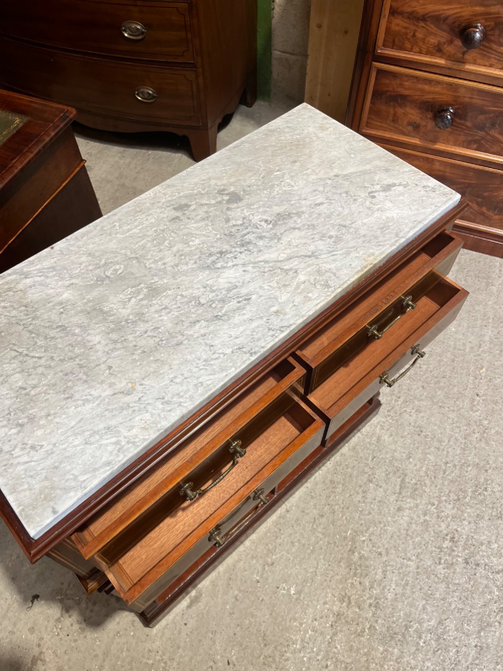 A late 19th-century inlaid mahogany cabinet featuring a grey marble surface, four drawers with string inlay and brass drop handles, above four vertical open storage divisions. View XIV