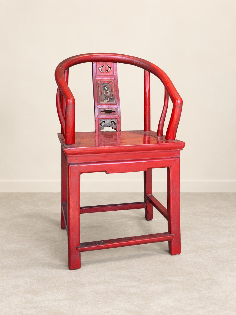 A traditional red lacquered Chinese armchair featuring a curved horseshoe backrest and a carved central splat.