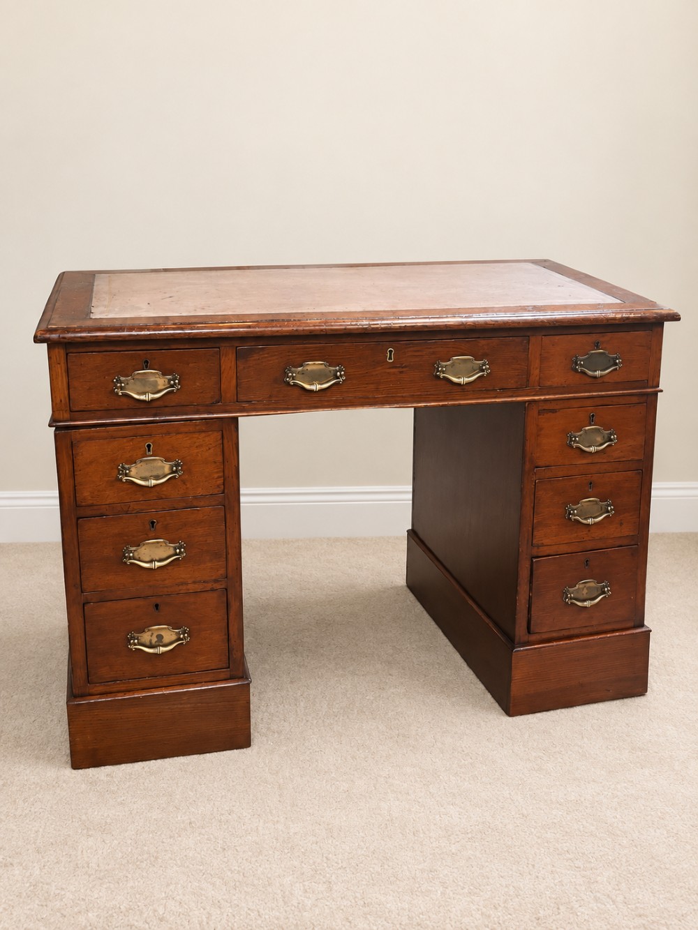 Late 19th-century oak pedestal desk featuring a tan leather-inset writing surface, nine drawers with brass handles, and solid plinth bases.