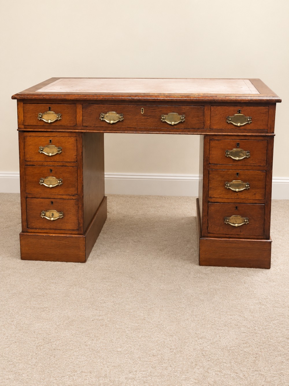 Late 19th-century oak pedestal desk featuring a tan leather-inset writing surface, nine drawers with brass handles, and solid plinth bases. View II