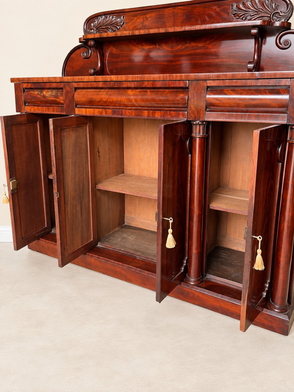 A 19th-century mahogany sideboard with a carved scrolled backboard, flame mahogany door panels, fluted columns, and a solid plinth base. View IV