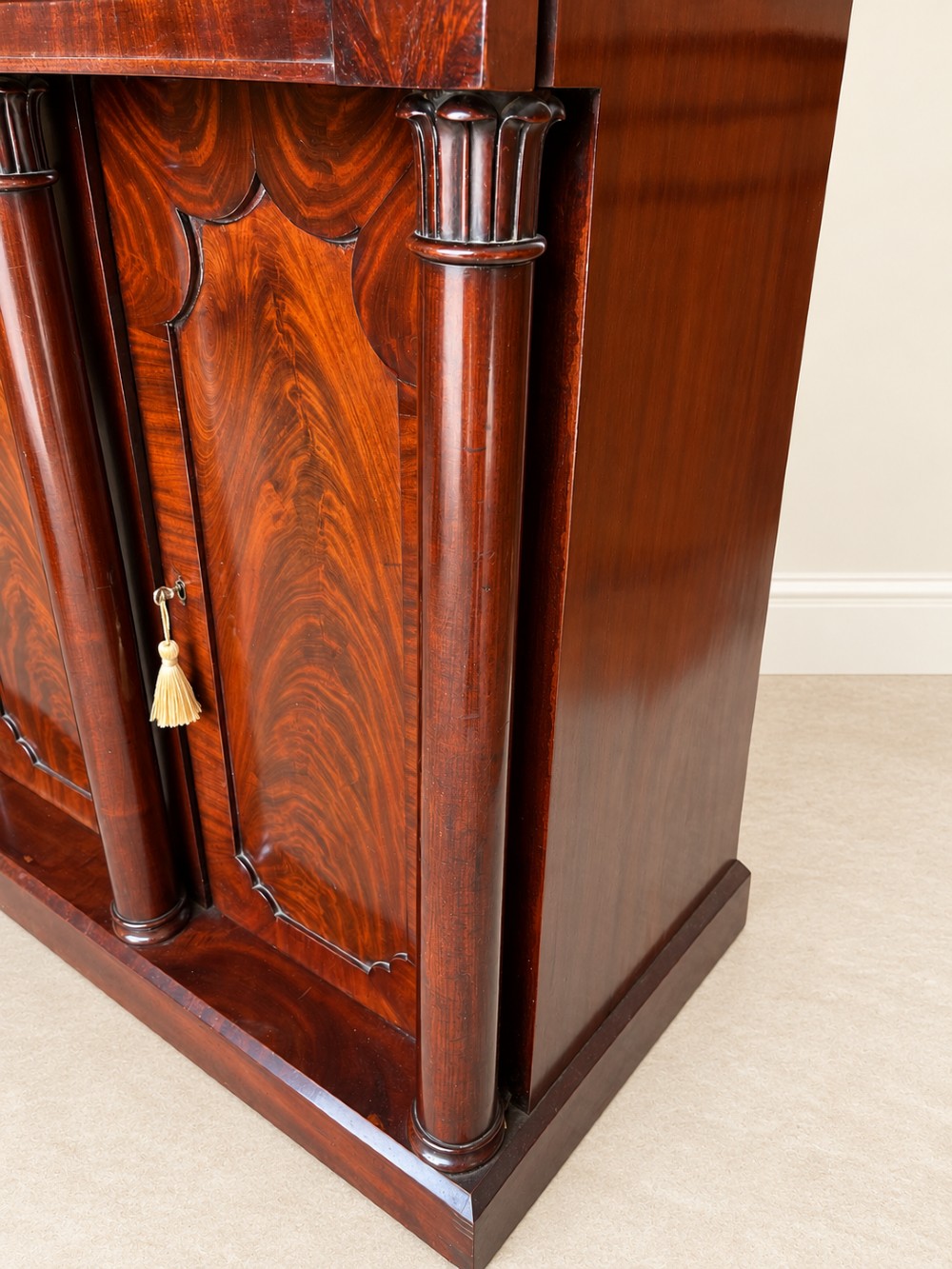 A 19th-century mahogany sideboard with a carved scrolled backboard, flame mahogany door panels, fluted columns, and a solid plinth base. View V