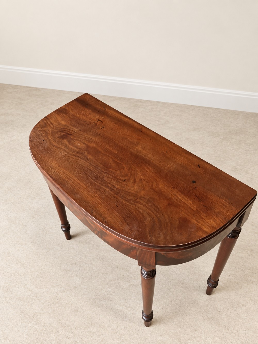 A Regency period mahogany fold-over table featuring a demilune top, flame mahogany frieze, and turned tapered legs with ring detailing. View III