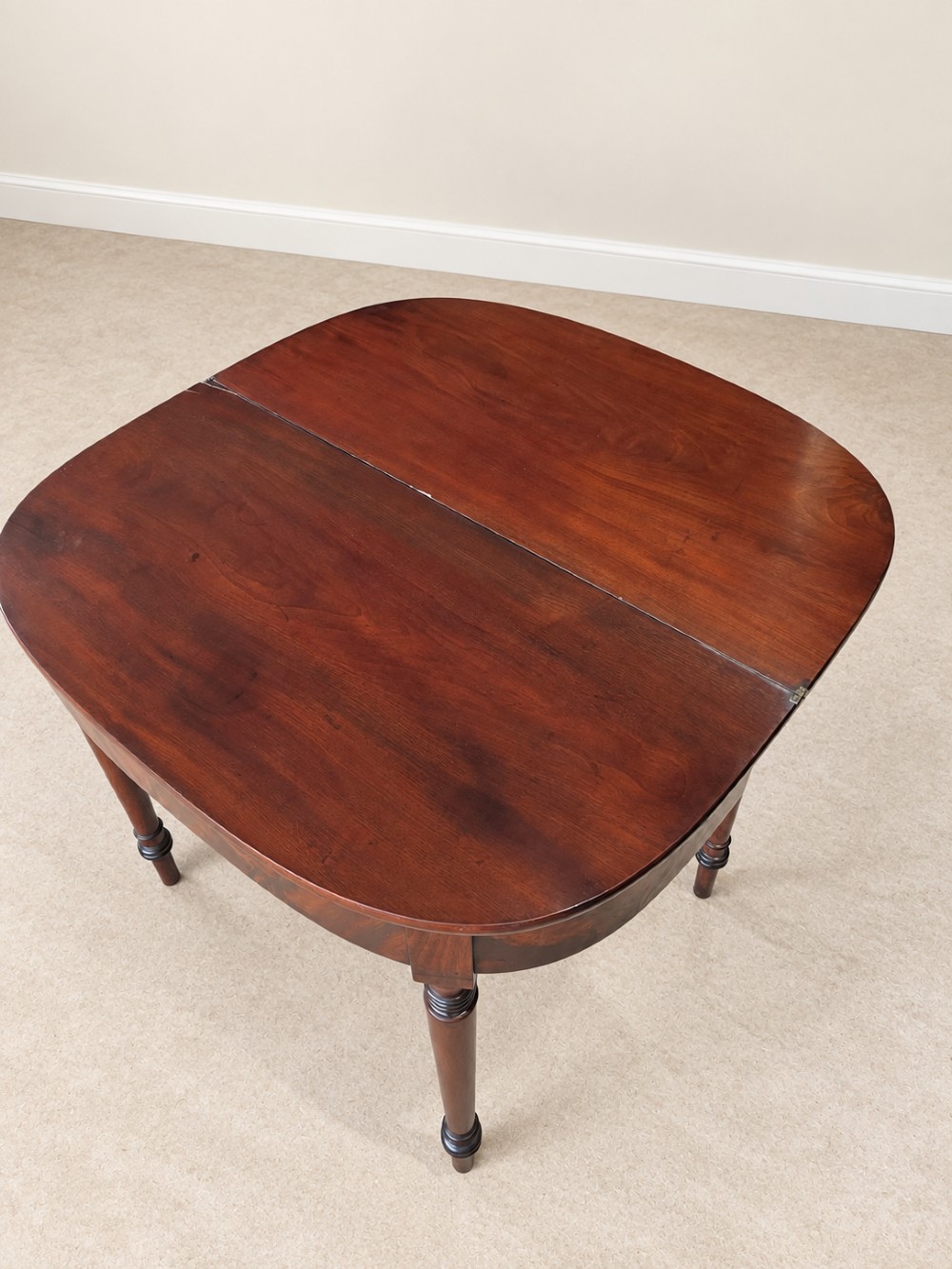 A Regency period mahogany fold-over table featuring a demilune top, flame mahogany frieze, and turned tapered legs with ring detailing. View VII