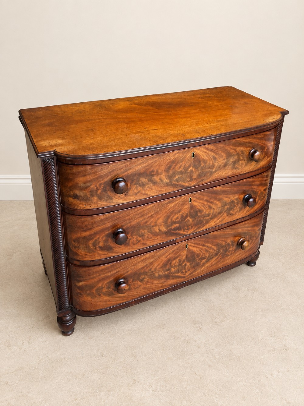 A Regency mahogany chest of drawers featuring a bowfront silhouette, three flame-veneered drawers with turned wooden handles, and reeded side columns. View III