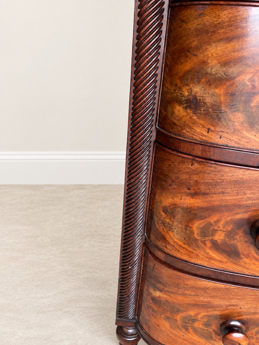 A Regency mahogany chest of drawers featuring a bowfront silhouette, three flame-veneered drawers with turned wooden handles, and reeded side columns. View IV