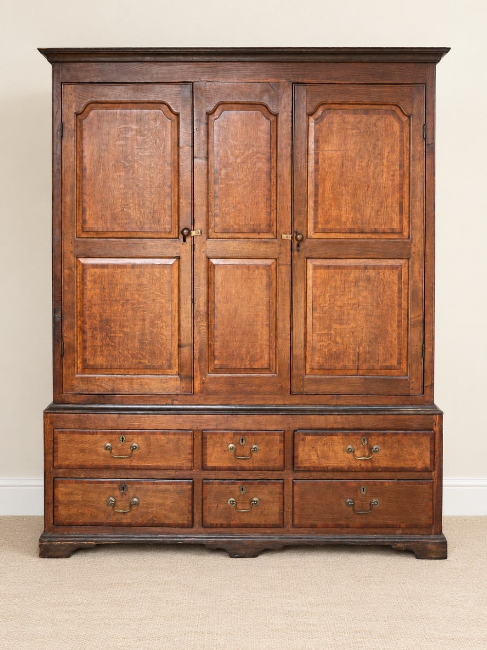 An early eighteenth-century warm brown oak housekeepers cupboard featuring three panelled upper doors over six lower drawers with brass drop handles.
