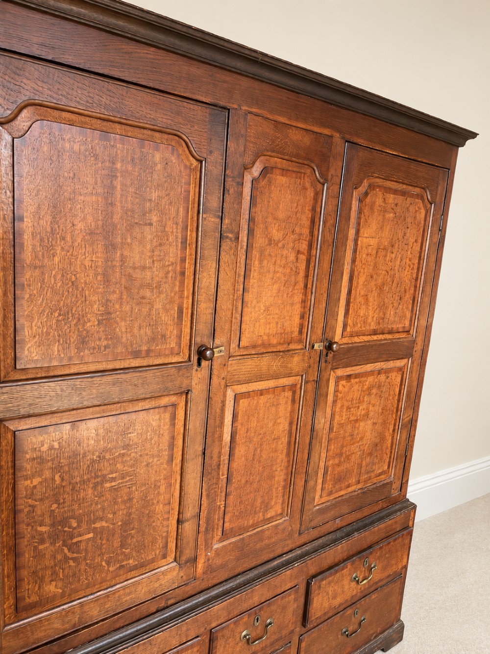 An early eighteenth-century warm brown oak housekeepers cupboard featuring three panelled upper doors over six lower drawers with brass drop handles. View II