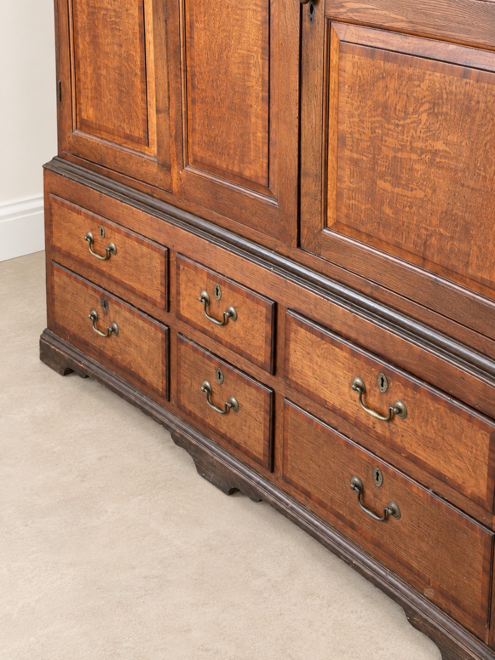 An early eighteenth-century warm brown oak housekeepers cupboard featuring three panelled upper doors over six lower drawers with brass drop handles. View III