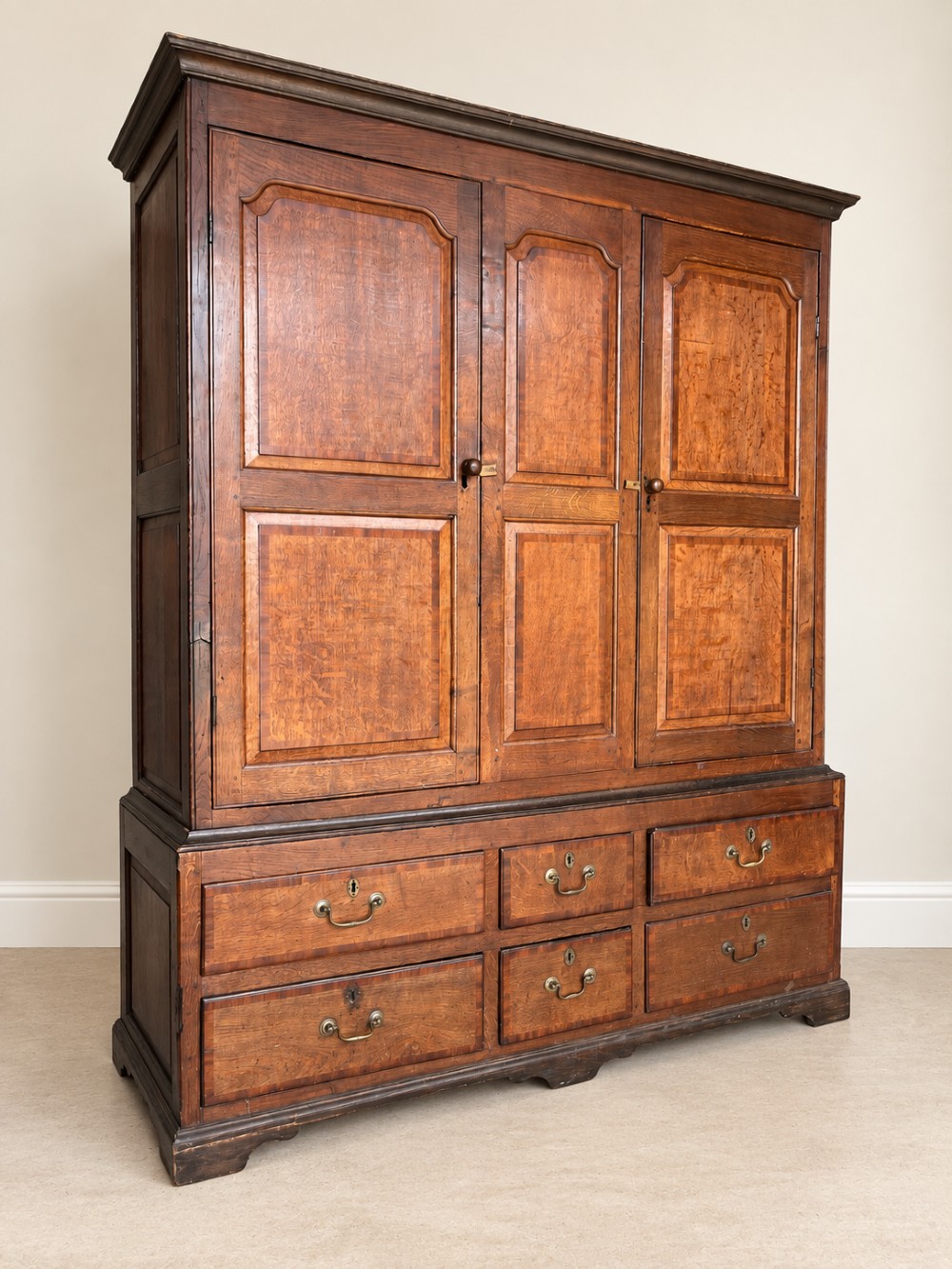 An early eighteenth-century warm brown oak housekeepers cupboard featuring three panelled upper doors over six lower drawers with brass drop handles. View IV