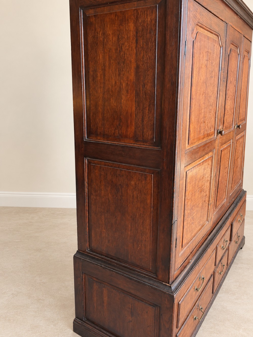 An early eighteenth-century warm brown oak housekeepers cupboard featuring three panelled upper doors over six lower drawers with brass drop handles. View V