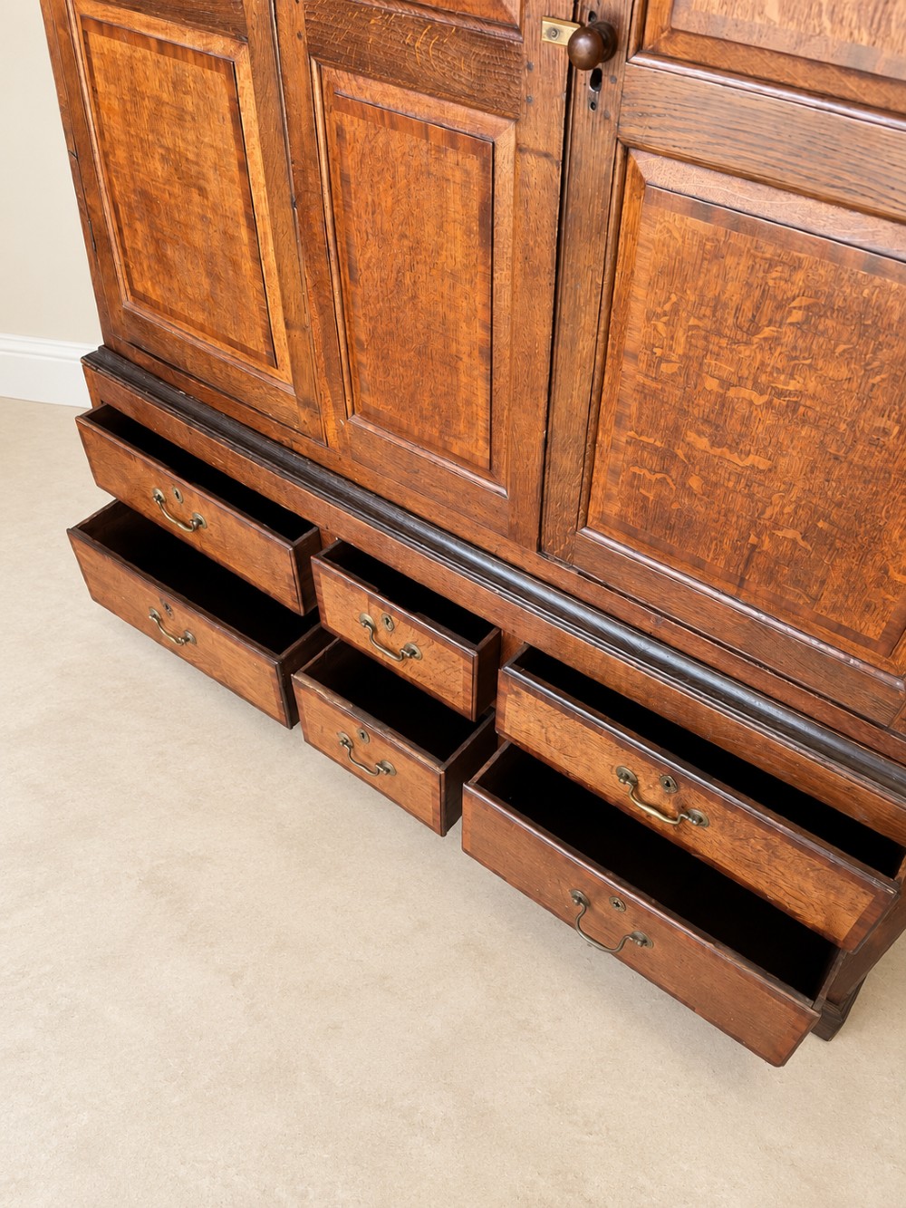 An early eighteenth-century warm brown oak housekeepers cupboard featuring three panelled upper doors over six lower drawers with brass drop handles. View VI