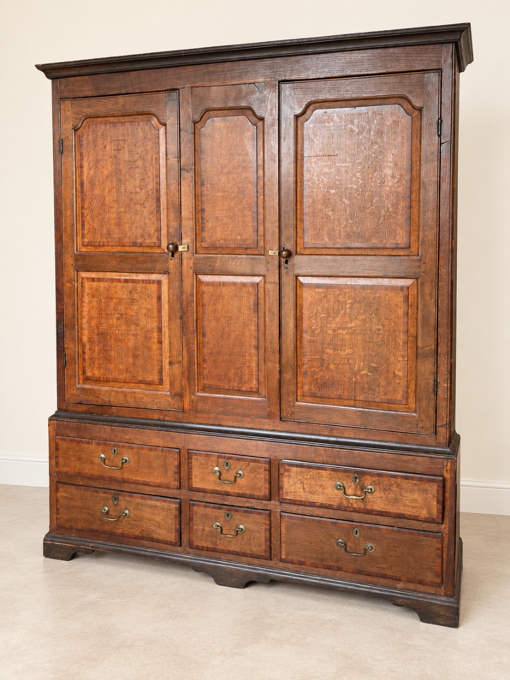 An early eighteenth-century warm brown oak housekeepers cupboard featuring three panelled upper doors over six lower drawers with brass drop handles. View VII
