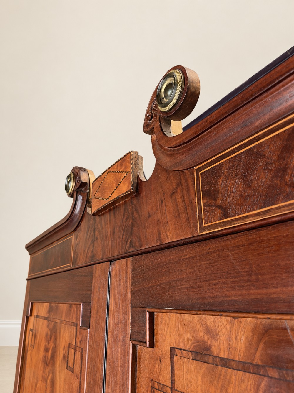 A Georgian mahogany cupboard on chest featuring upper double panelled doors with flame veneer, decorative cresting, and a lower chest of drawers on turned feet. View III