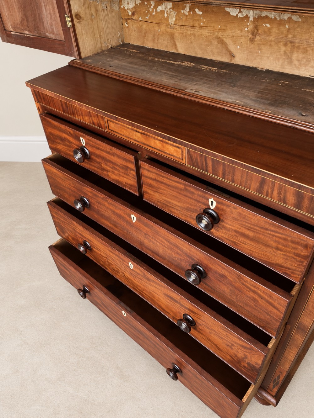 A Georgian mahogany cupboard on chest featuring upper double panelled doors with flame veneer, decorative cresting, and a lower chest of drawers on turned feet. View V