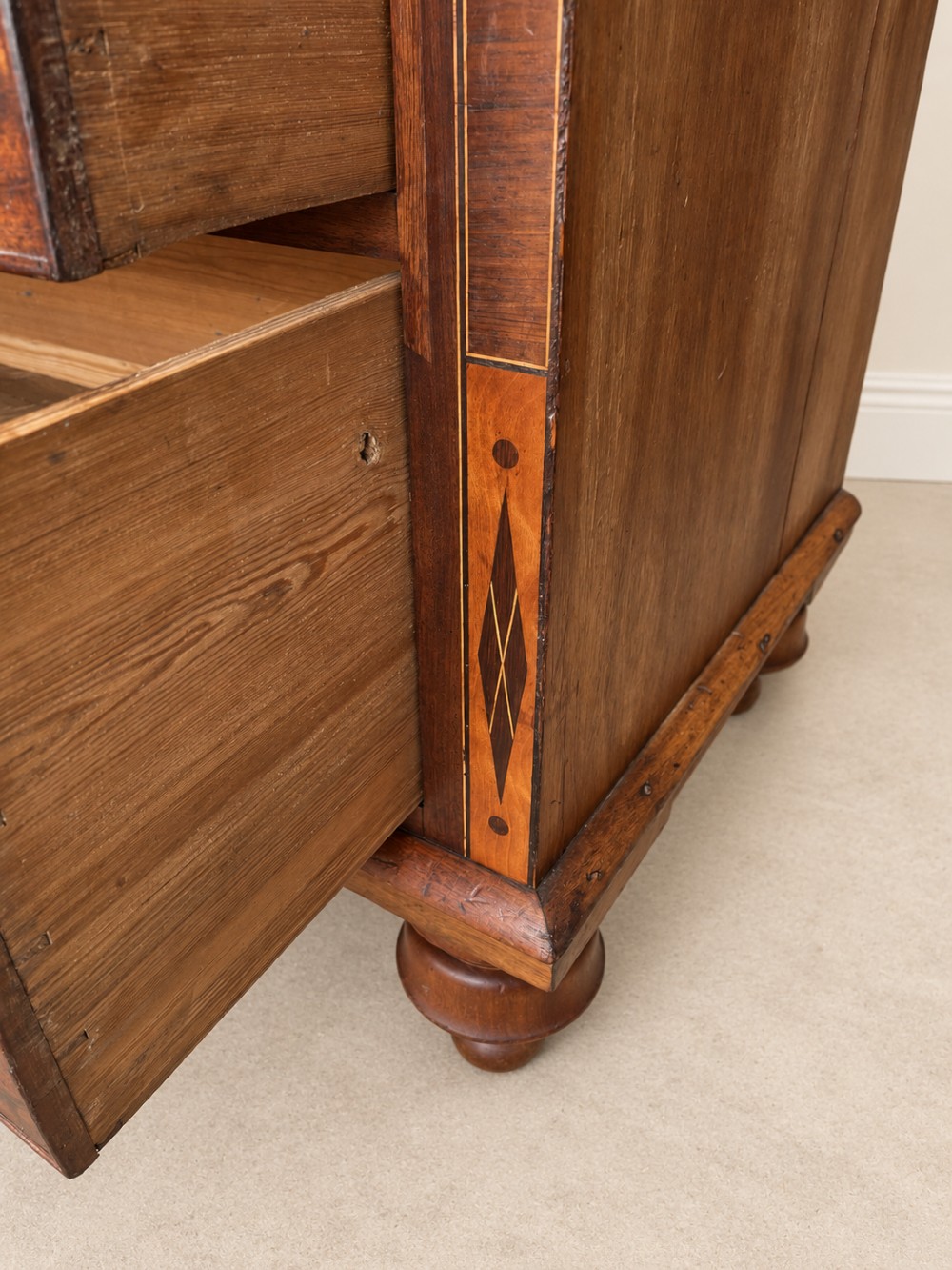 A Georgian mahogany cupboard on chest featuring upper double panelled doors with flame veneer, decorative cresting, and a lower chest of drawers on turned feet. View VI