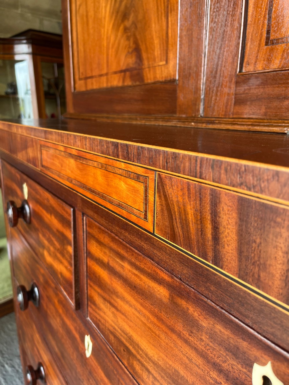 A Georgian mahogany cupboard on chest featuring upper double panelled doors with flame veneer, decorative cresting, and a lower chest of drawers on turned feet. View IX