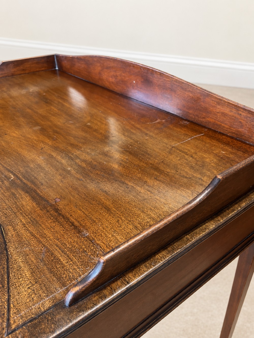 A Georgian style mahogany side table featuring a curved front apron, two drawers with brass swan-neck handles, a low shaped gallery back, and square tapered legs on castors. View V
