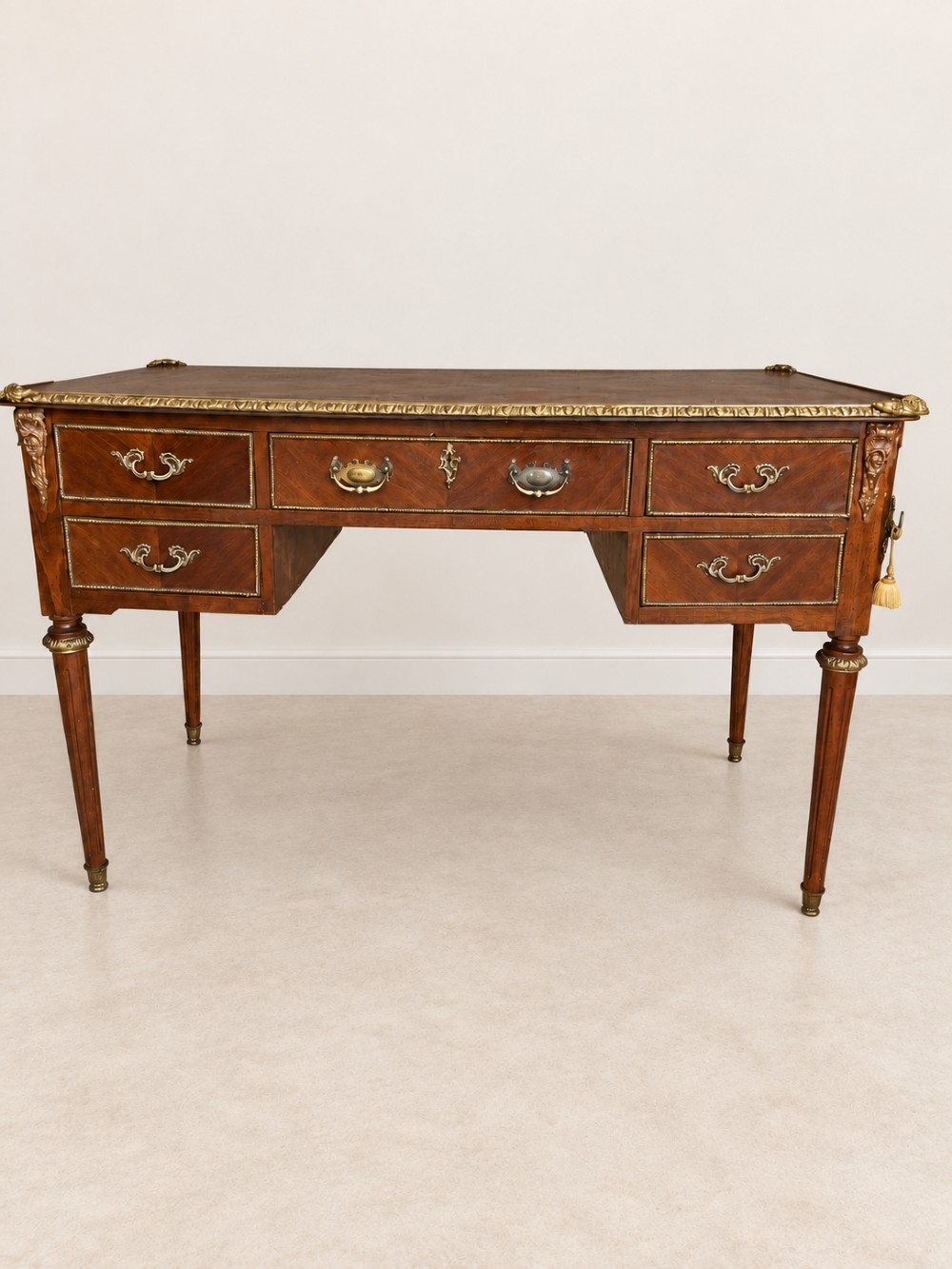 A French Louis XVI style mahogany writing desk featuring a brown leather top, five drawers with cast brass handles, and gilt bronze mounts on fluted tapering legs. View II