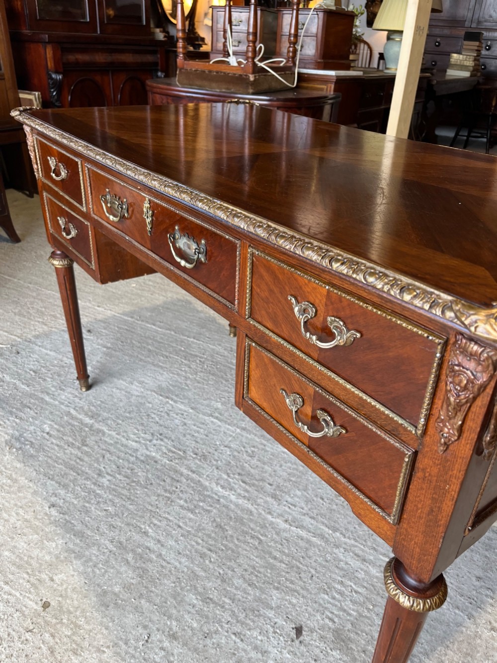 A French Louis XVI style mahogany writing desk featuring a brown leather top, five drawers with cast brass handles, and gilt bronze mounts on fluted tapering legs. View III