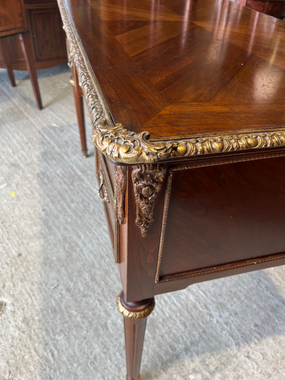 A French Louis XVI style mahogany writing desk featuring a brown leather top, five drawers with cast brass handles, and gilt bronze mounts on fluted tapering legs. View V