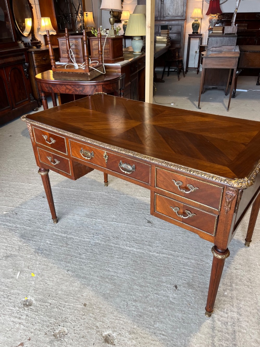 A French Louis XVI style mahogany writing desk featuring a brown leather top, five drawers with cast brass handles, and gilt bronze mounts on fluted tapering legs. View VII