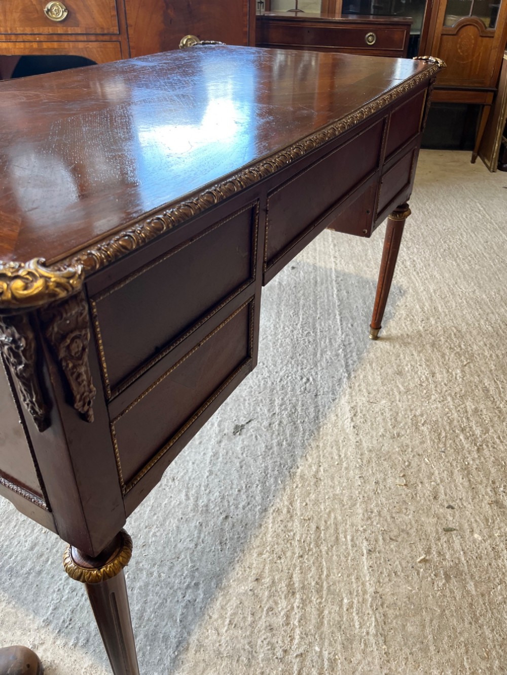 A French Louis XVI style mahogany writing desk featuring a brown leather top, five drawers with cast brass handles, and gilt bronze mounts on fluted tapering legs. View IX