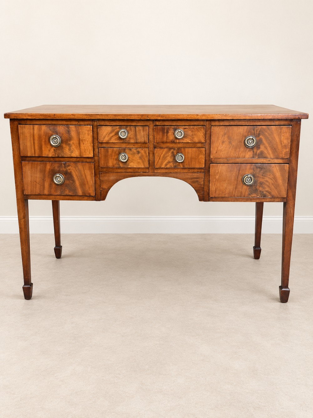 A 19th-century mahogany sideboard featuring eight drawer fronts, circular brass handles, an arched central kneehole, and tapered legs ending in spade feet. View II