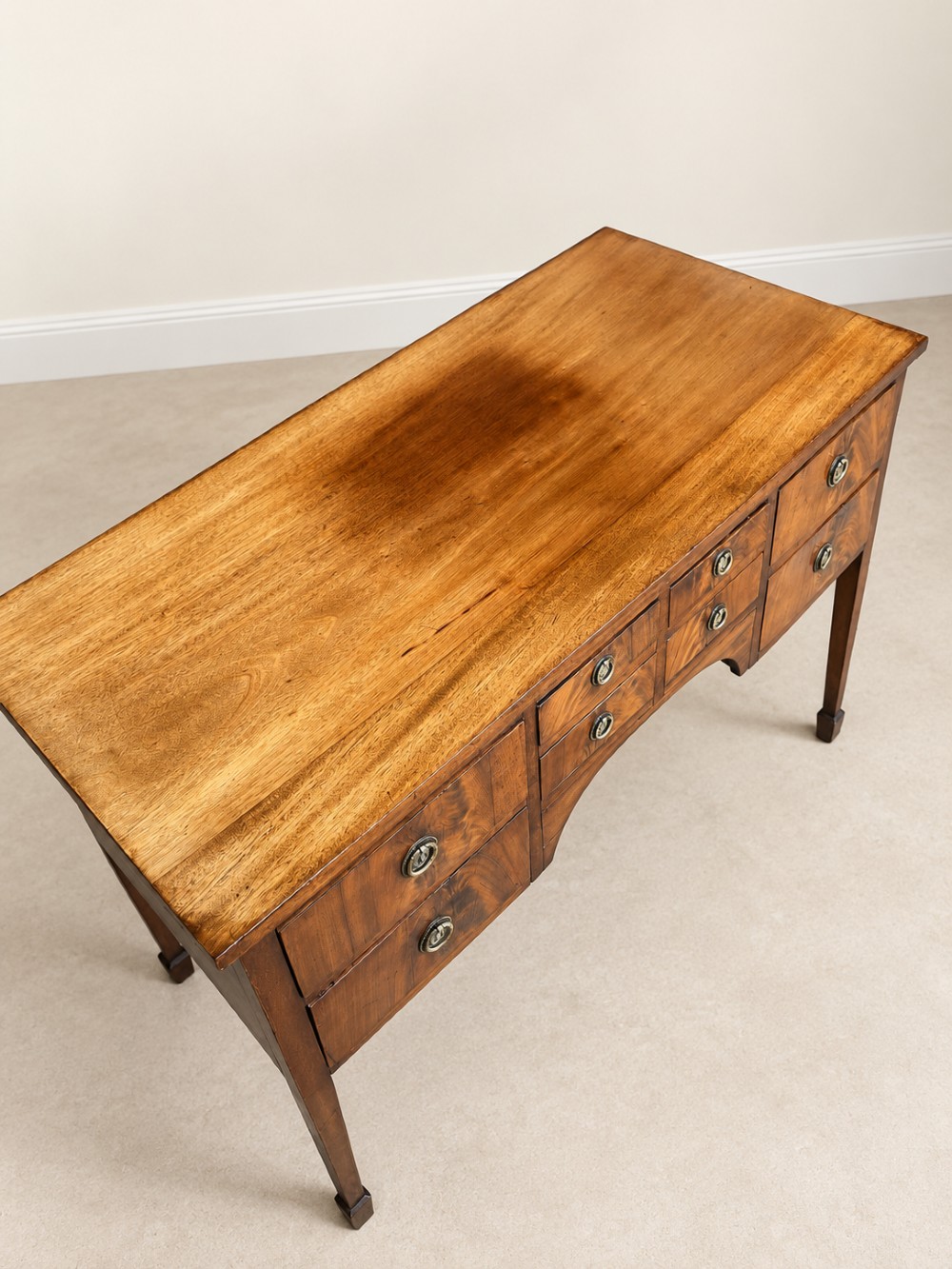 A 19th-century mahogany sideboard featuring eight drawer fronts, circular brass handles, an arched central kneehole, and tapered legs ending in spade feet. View III