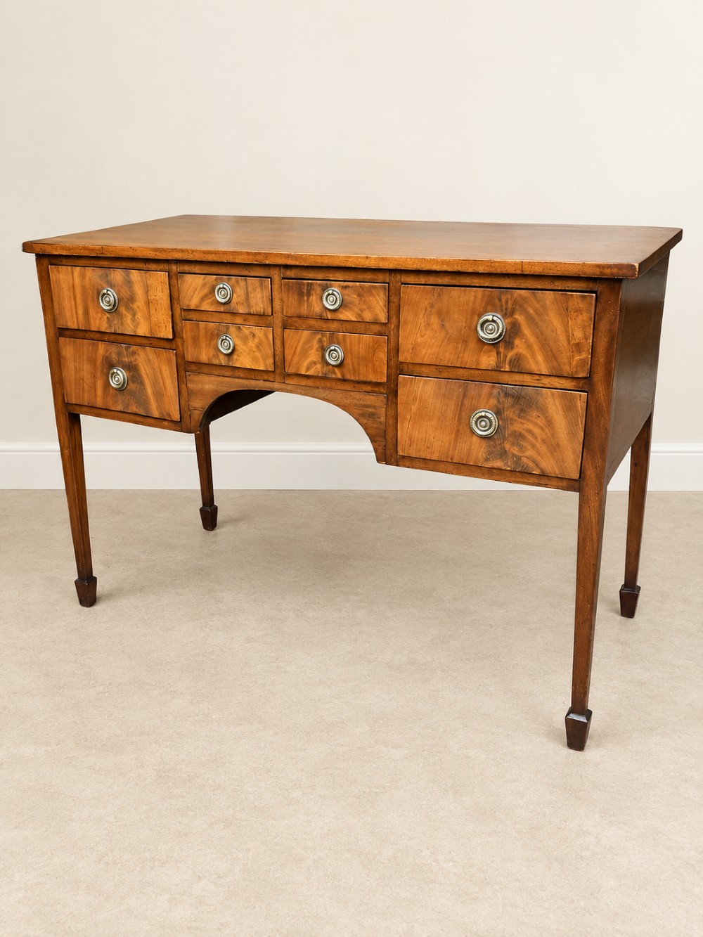 A 19th-century mahogany sideboard featuring eight drawer fronts, circular brass handles, an arched central kneehole, and tapered legs ending in spade feet. View IV