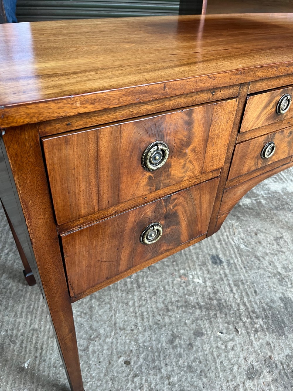 A 19th-century mahogany sideboard featuring eight drawer fronts, circular brass handles, an arched central kneehole, and tapered legs ending in spade feet. View V