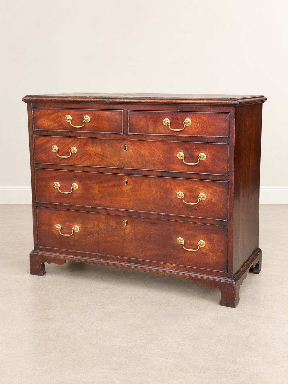 A Georgian mahogany chest of drawers featuring two short drawers above three long drawers with brass swan-neck handles, raised on bracket feet. View II