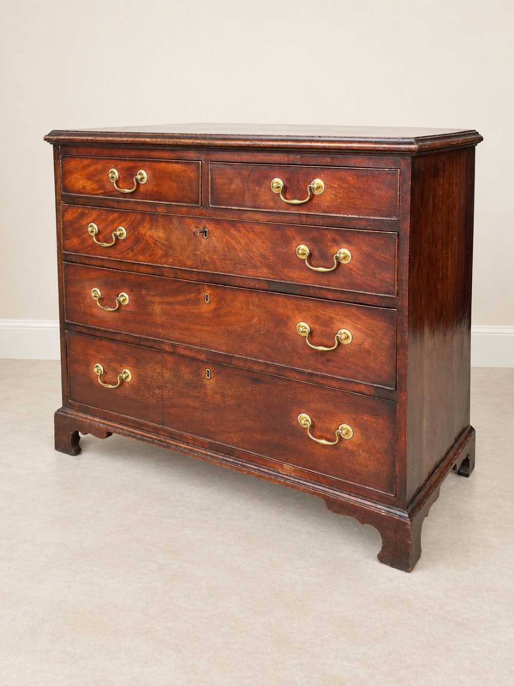 A Georgian mahogany chest of drawers featuring two short drawers above three long drawers with brass swan-neck handles, raised on bracket feet. View IV
