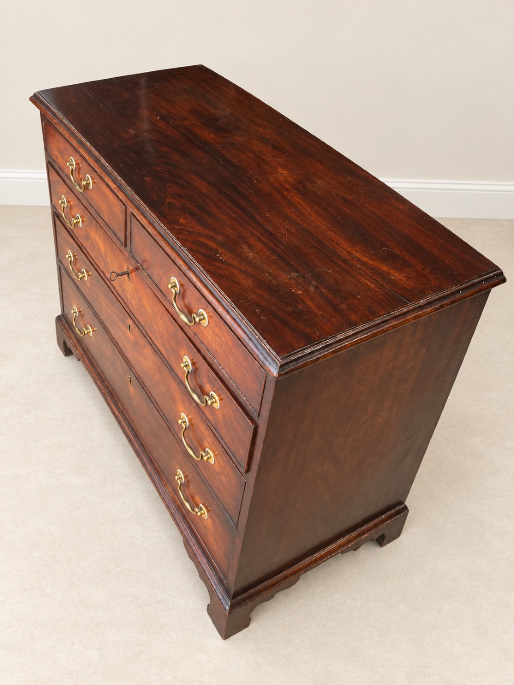 A Georgian mahogany chest of drawers featuring two short drawers above three long drawers with brass swan-neck handles, raised on bracket feet. View V