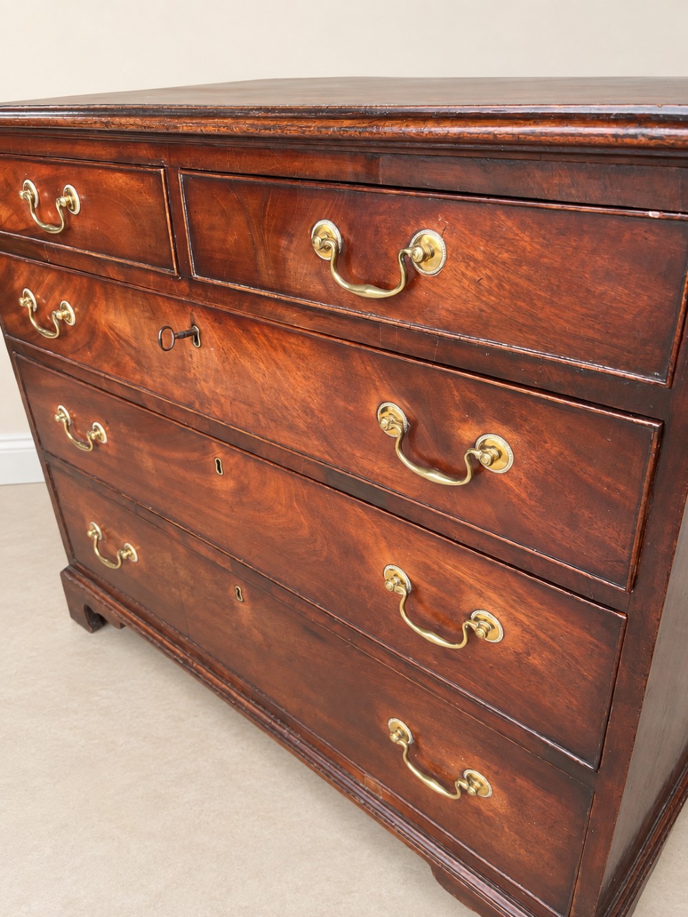 A Georgian mahogany chest of drawers featuring two short drawers above three long drawers with brass swan-neck handles, raised on bracket feet. View VI